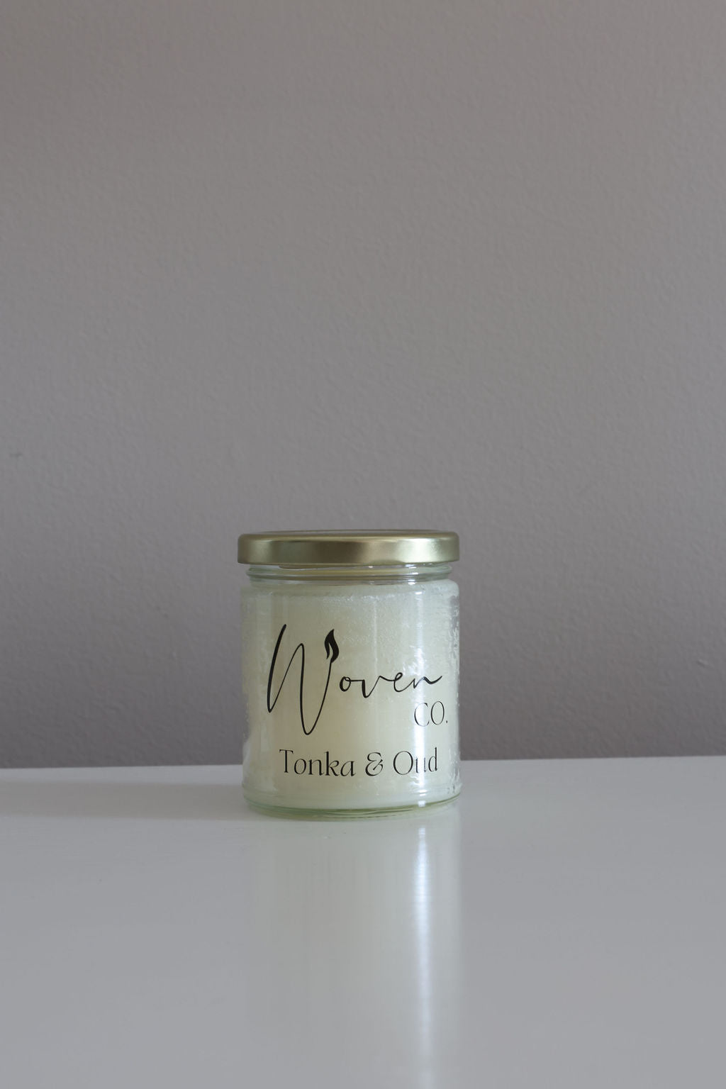 Jar of candle labeled 'Woven Co' on a plain background