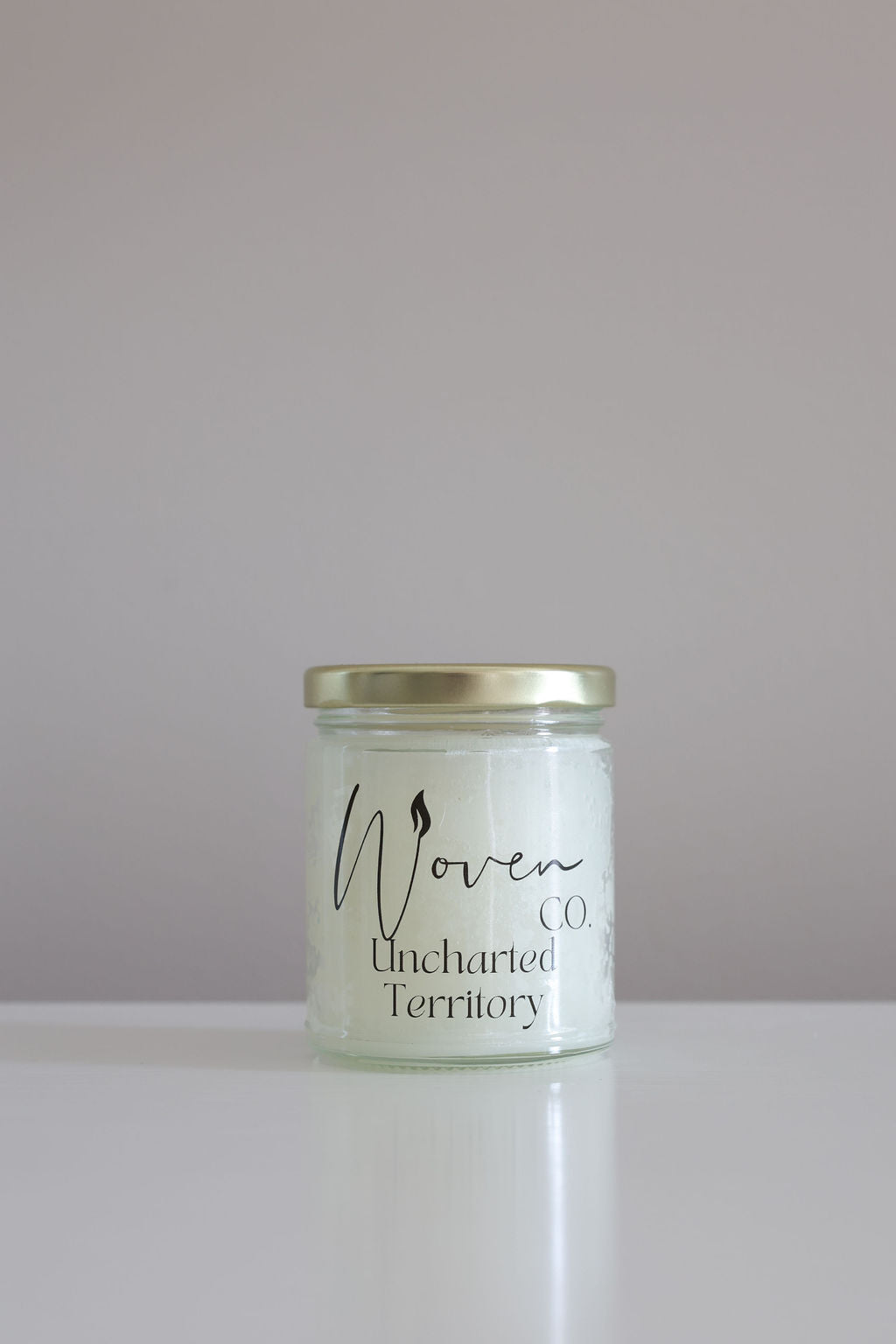 Jar of candle with 'Woven Co' and 'Uncharted Territory' text on a light background